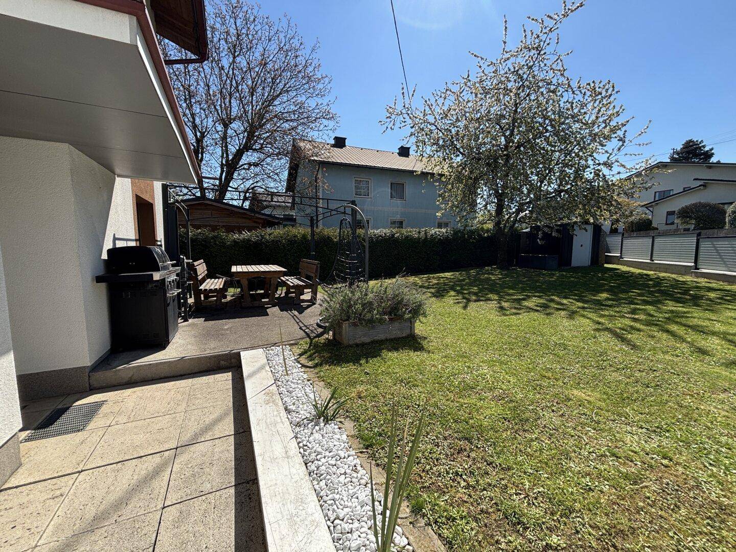 Gepflegter Garten mit Rasenfläche, Grillplatz und Sitzgelegenheiten im Freien.