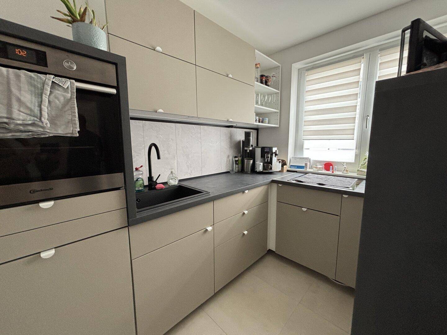 Moderne Küche in Beige mit integriertem Backofen und Fenster für Tageslicht.