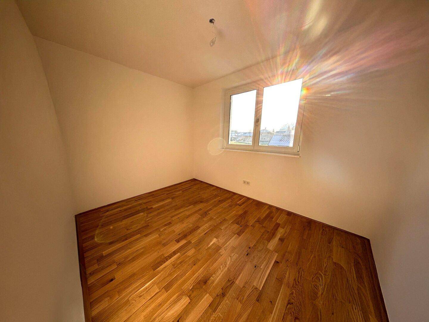 Sonniges Schlafzimmer mit Holzparkettboden und großem Fenster für viel Licht.