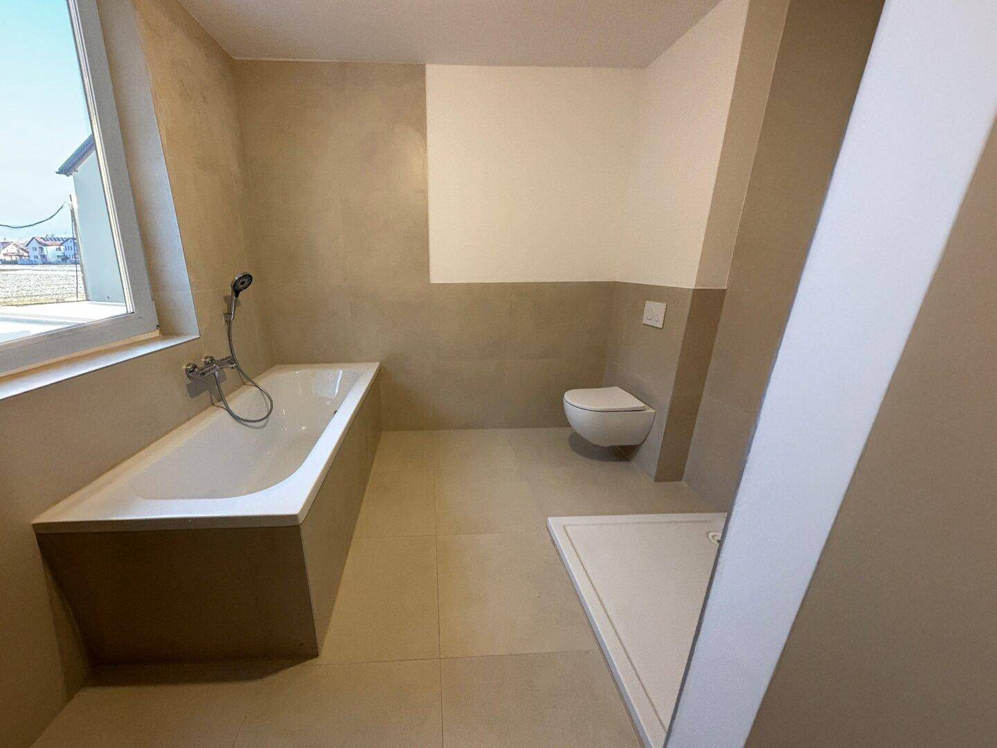 Modernes Badezimmer mit Badewanne, Dusche und Wand-WC in neutralen Farbtönen.