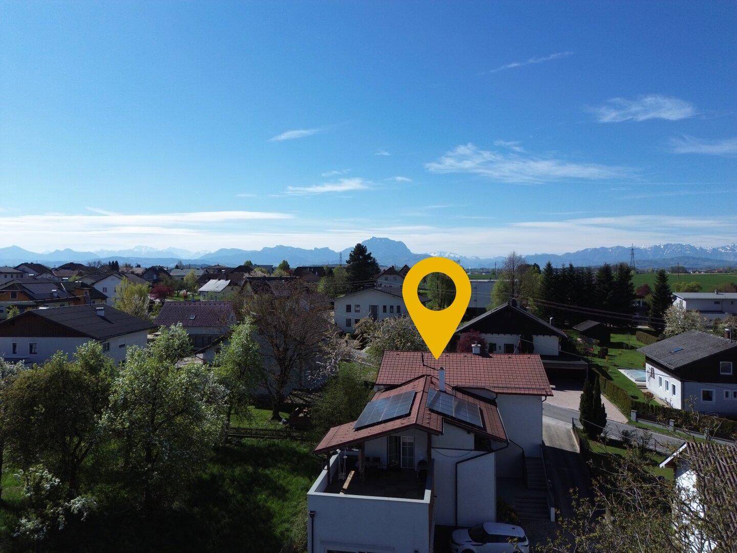 Luftaufnahme eines Hauses mit Solaranlage und weitem Blick auf die umliegende Landschaft und die Alpen.
