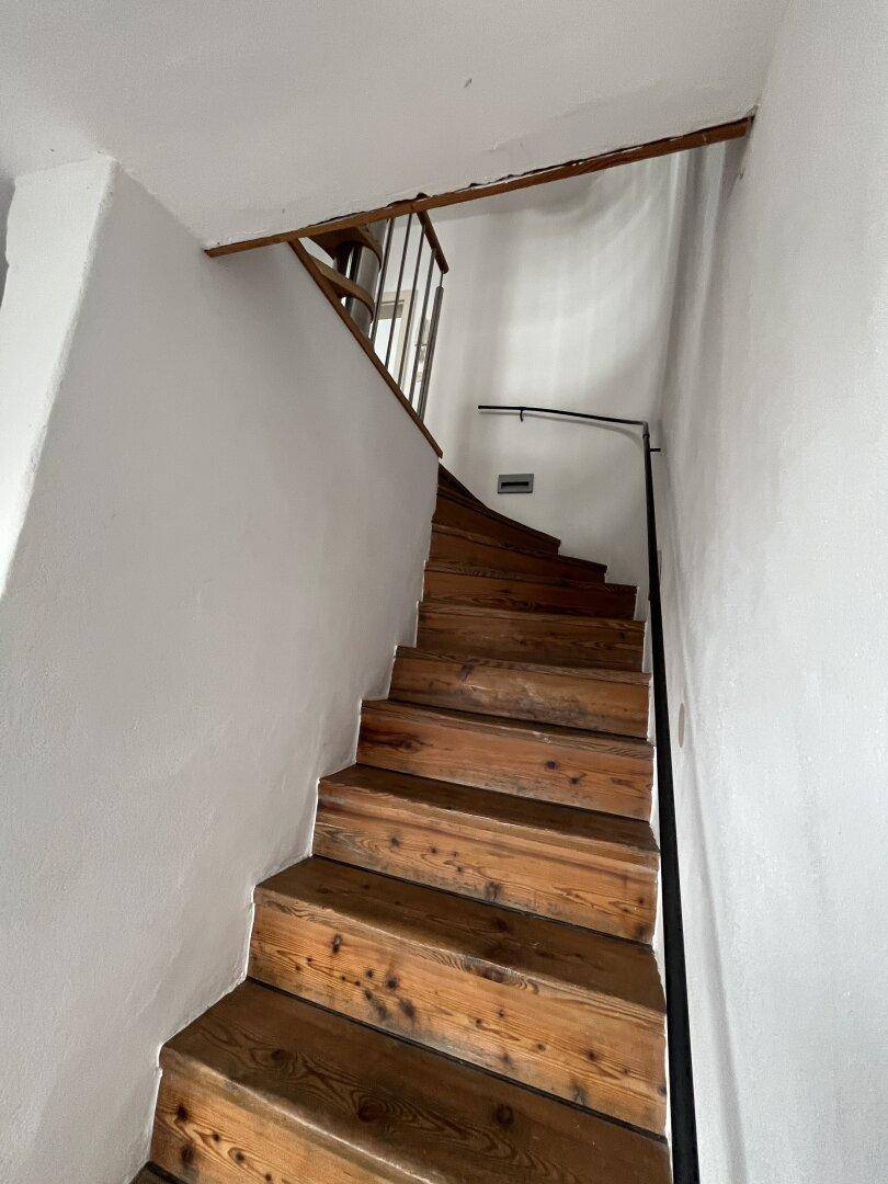 Rustikale Holztreppe mit schlichten weißen Wänden, die in die obere Etage führt.