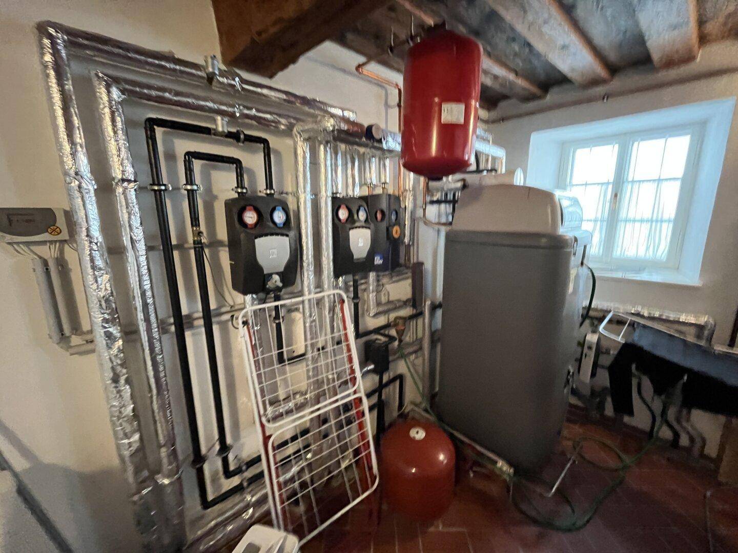 Heizungsraum mit moderner Anlagentechnik, isolierten Rohren und einem Fenster.