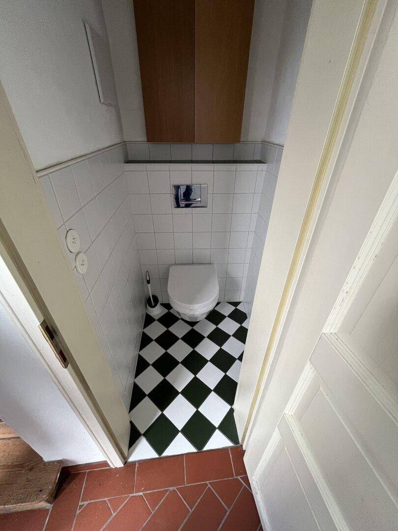 Kleines Gäste-WC mit weiß gefliesten Wänden und schwarz-weißem Schachbrettmuster auf dem Boden.