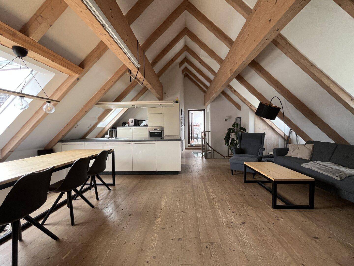 Großzügiger offener Wohn- und Essbereich mit Küche, Holzbalken und viel natürlichem Licht.