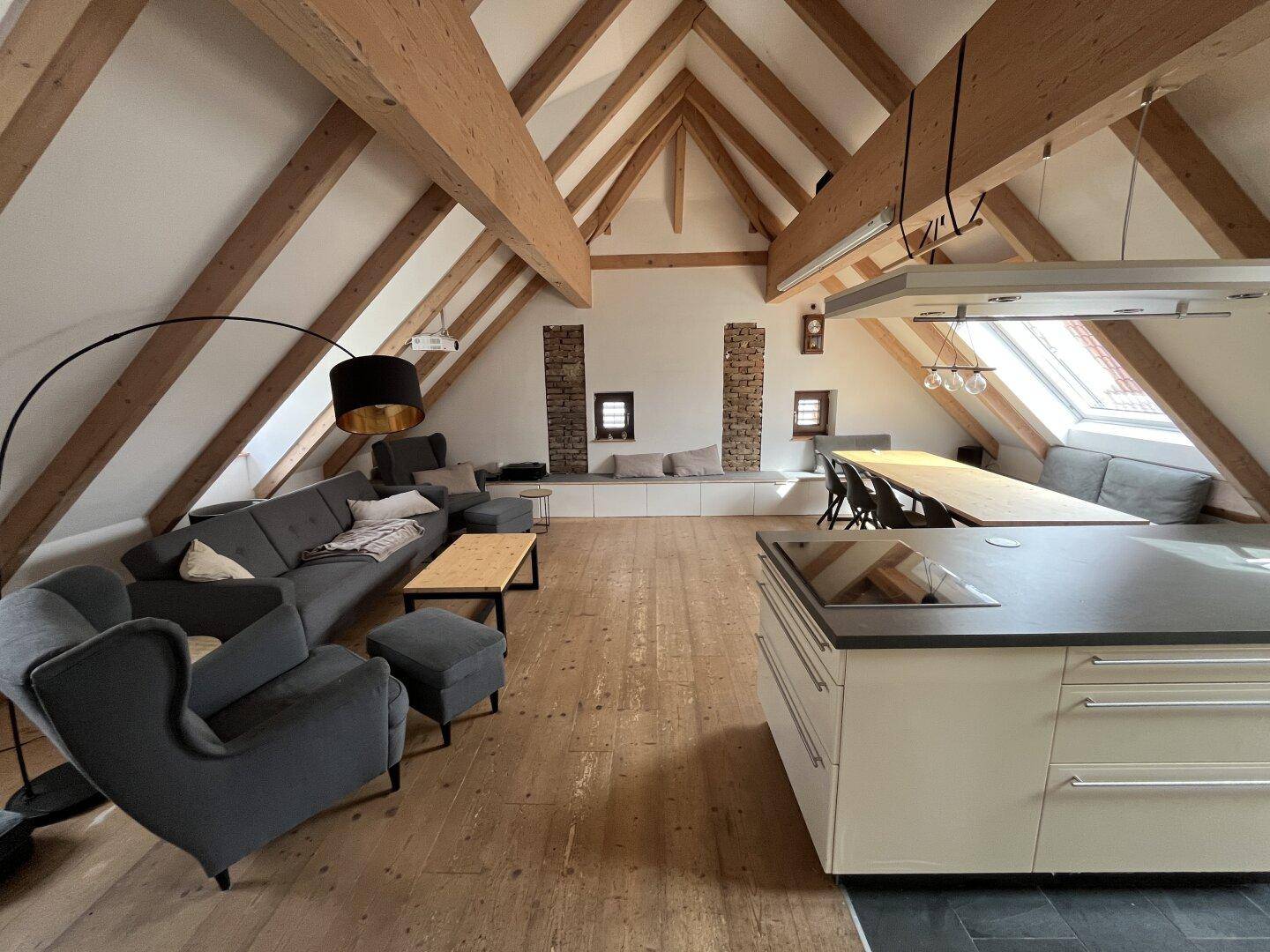 Geräumiges Dachgeschoss-Apartment mit offener Küche, Essbereich und gemütlichem Wohnbereich unter sichtbaren Holzbalken.