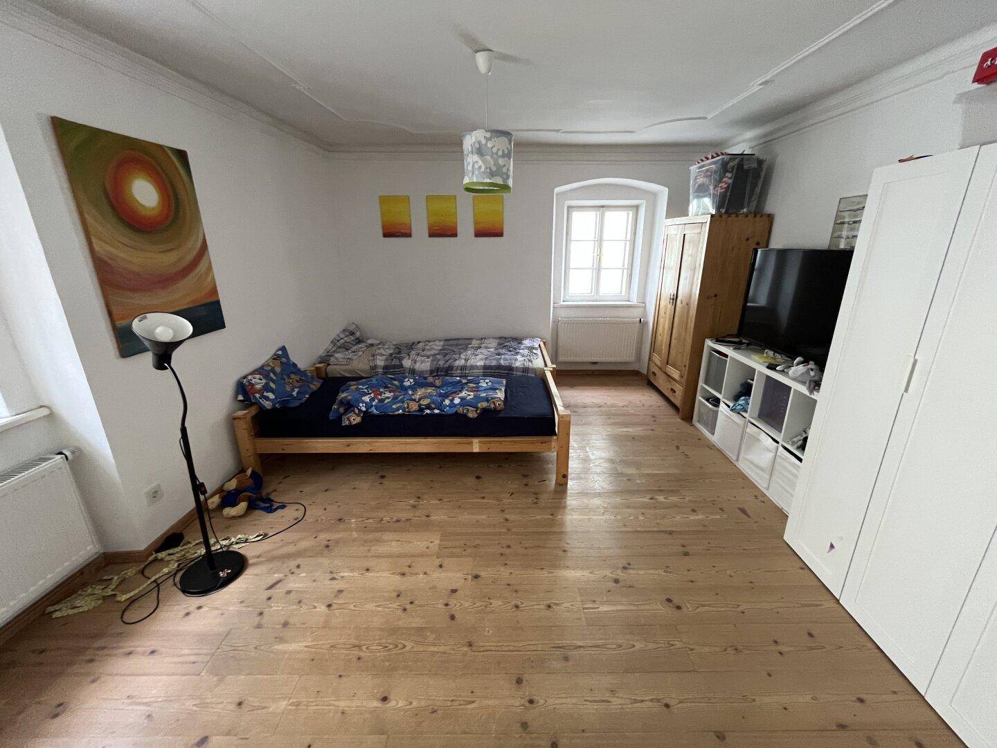 Gemütliches Schlafzimmer mit Holzboden, Bett und Kleiderschrank, hell durch das Fenster.