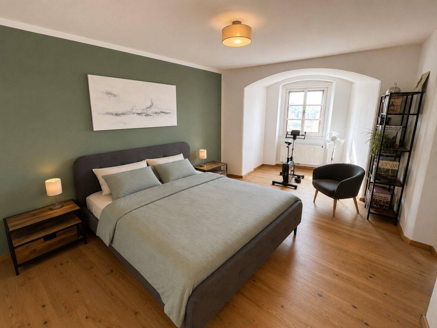 Modernes Schlafzimmer mit großem Bett, grüner Akzentwand und warmem Holzboden.
