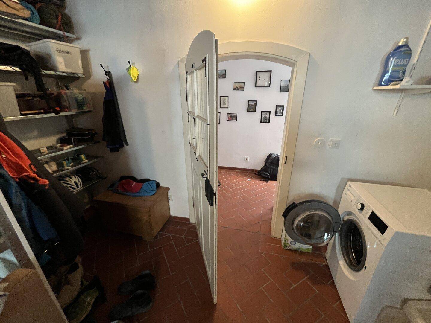 Praktischer Hauswirtschaftsraum mit Waschmaschine, Regalen und Terrakotta-Fliesenboden.