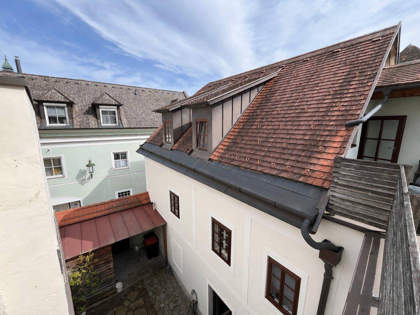Blick von oben auf die historische Gebäudefassade mit roten Ziegeldächern und einem kleinen Innenhof.