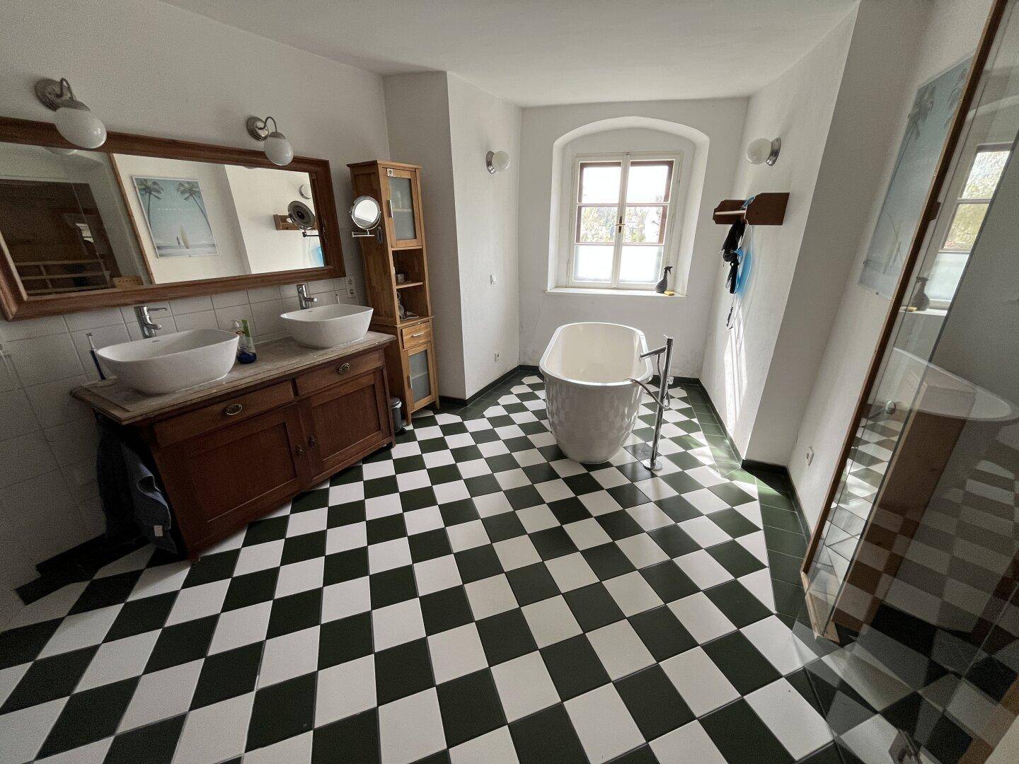 Geräumiges Badezimmer mit freistehender Badewanne, Doppelwaschbecken und schwarz-weißem Fliesenboden.