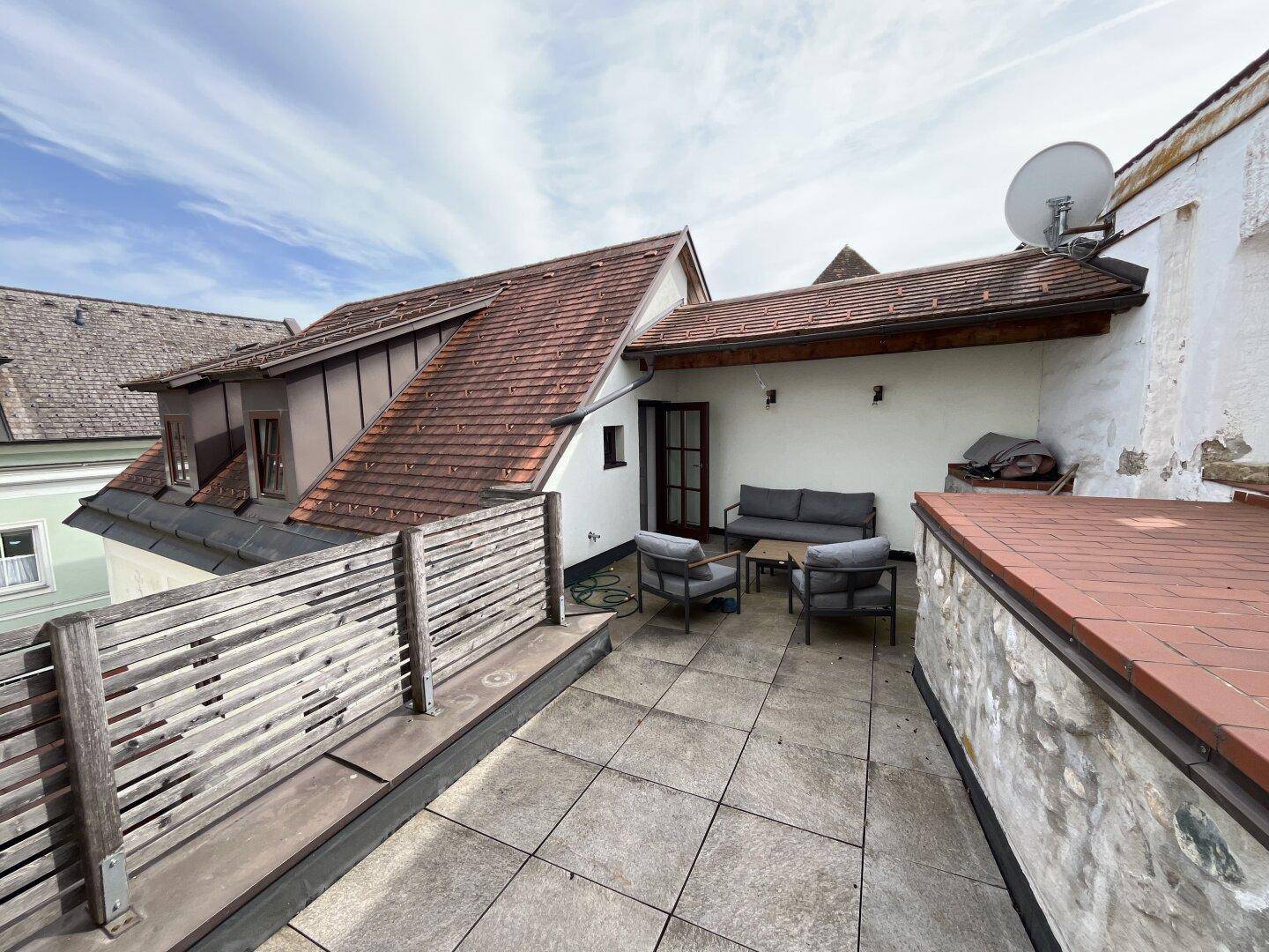 Große geflieste Dachterrasse mit bequemen Gartenmöbeln und Blick auf die umliegenden Dächer.