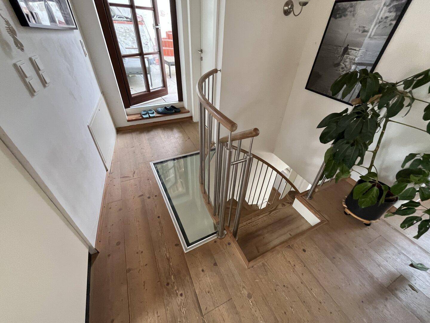 Moderne Treppe mit Glasboden und Holzstufen, die zu einem Außenbereich führt.