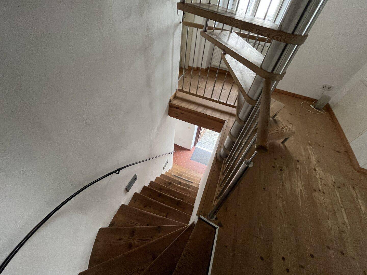 Blick von oben auf die Holztreppe, die zu den unteren Etagen mit Holzboden führt.