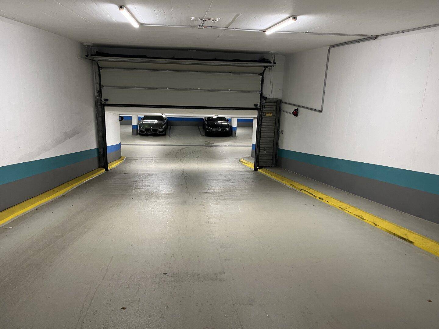 Ausfahrt der Tiefgarage mit Rolltor und weiteren Stellplätzen im Hintergrund des Gebäudes.