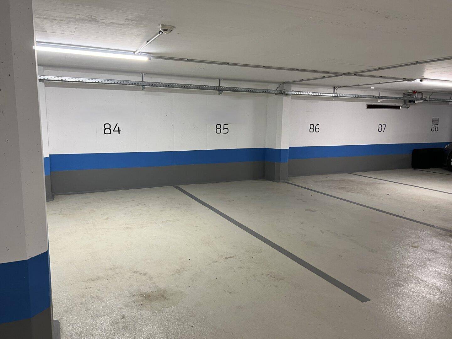 Leere Stellplätze in der Tiefgarage, sauber und gut beleuchtet mit blauen Akzenten an den Wänden.