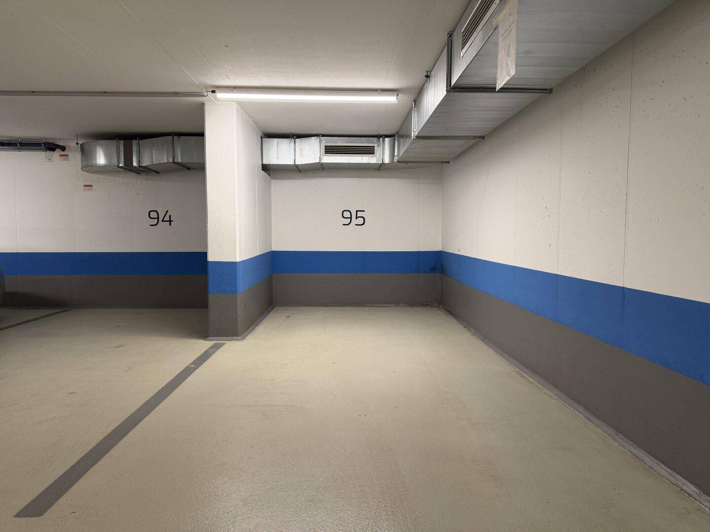 Weitere leere Stellplätze in der Tiefgarage mit sichtbaren Lüftungskanälen an der Decke.