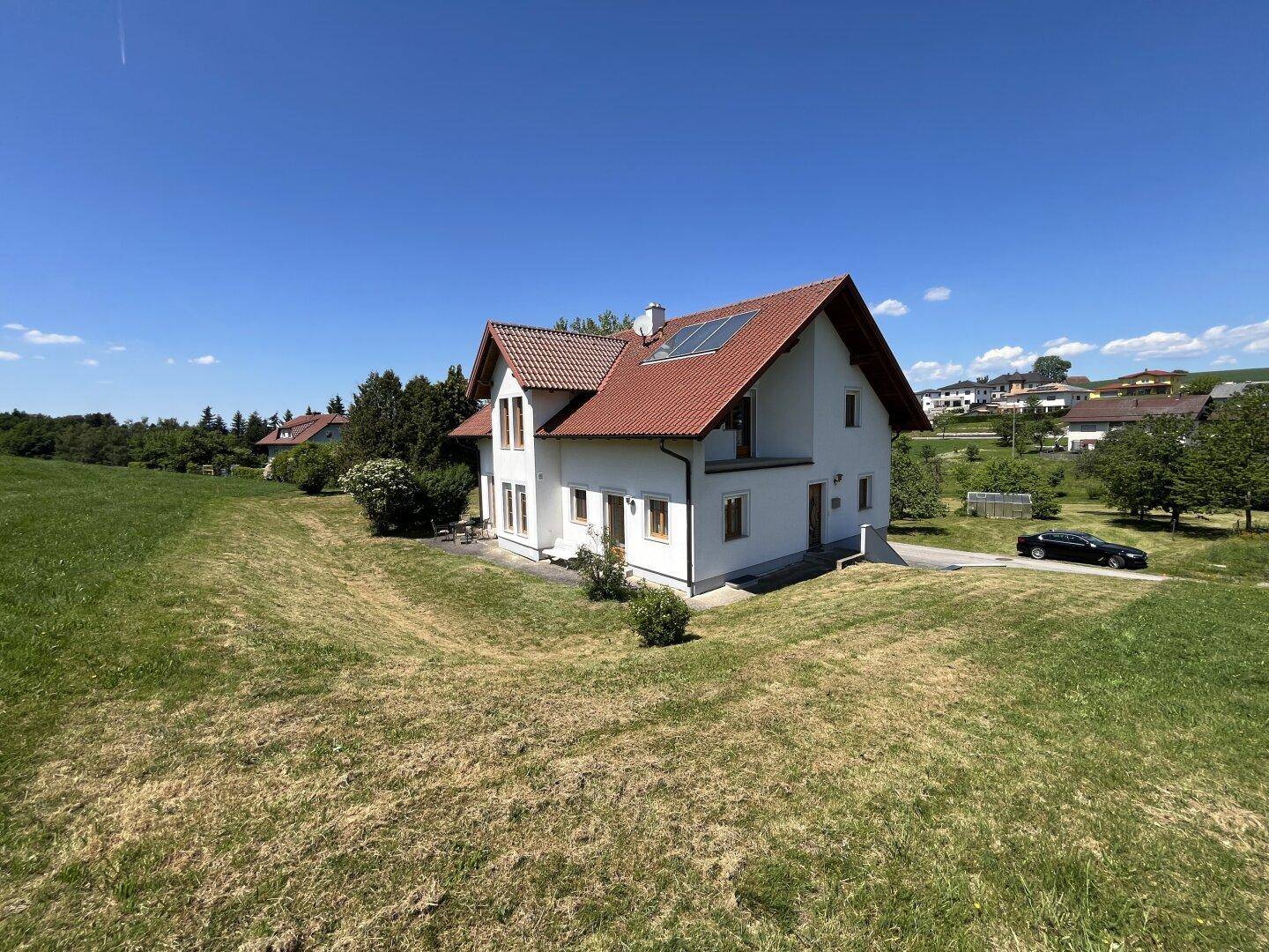 Freistehendes Einfamilienhaus mit rotem Ziegeldach und Solaranlage in ländlicher Umgebung.