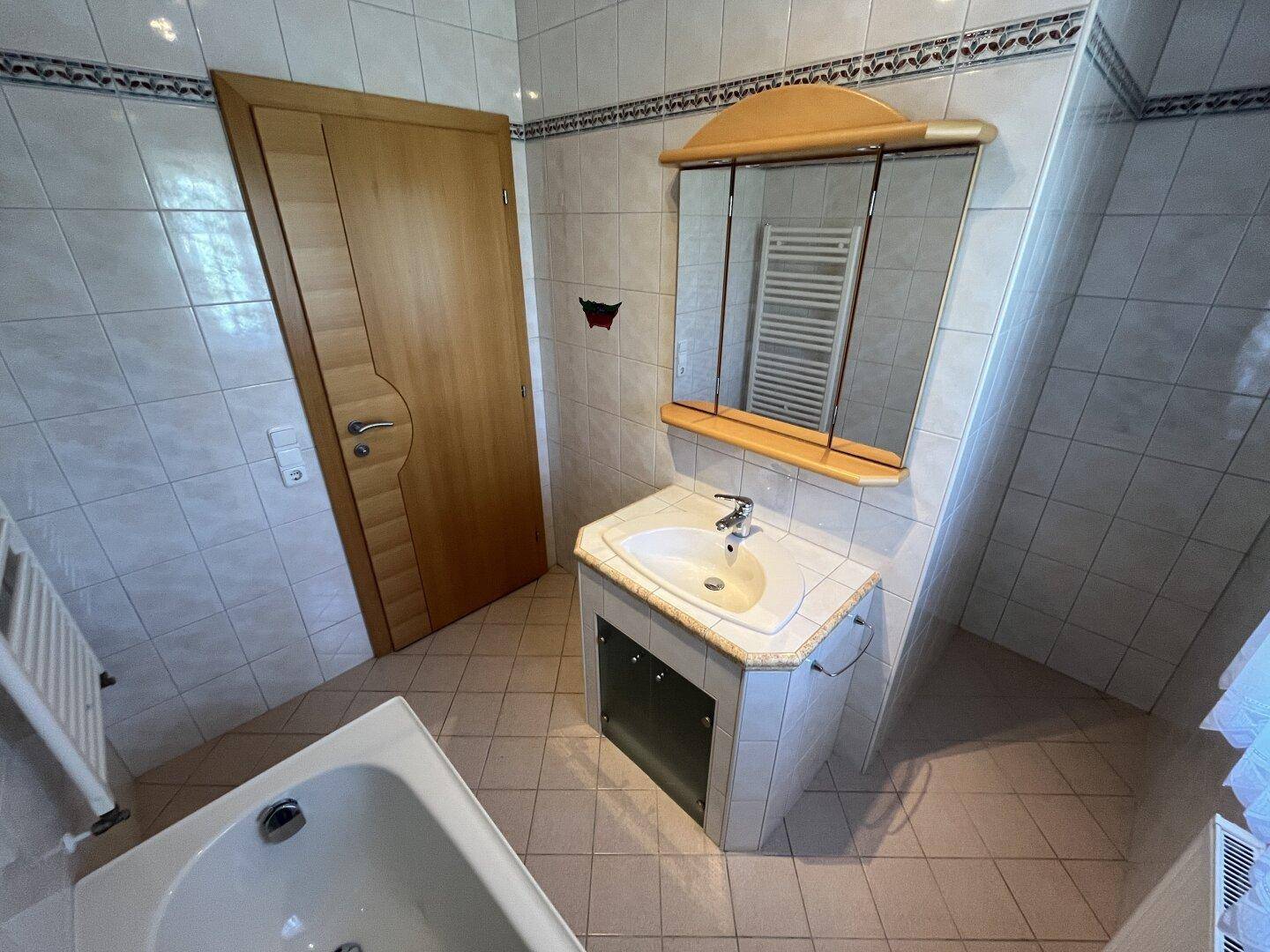 Helles Badezimmer mit Badewanne, Waschbecken, Spiegelschrank und beheiztem Handtuchhalter.