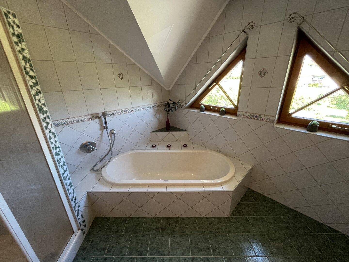Badezimmer mit Eckbadewanne, grünen Fliesen und schrägen Dachfenstern.