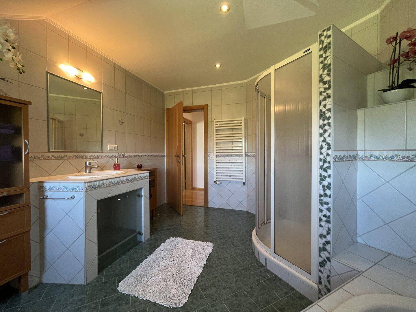 Geräumiges Badezimmer mit Dusche, Einzelwaschbecken und beheiztem Handtuchhalter.