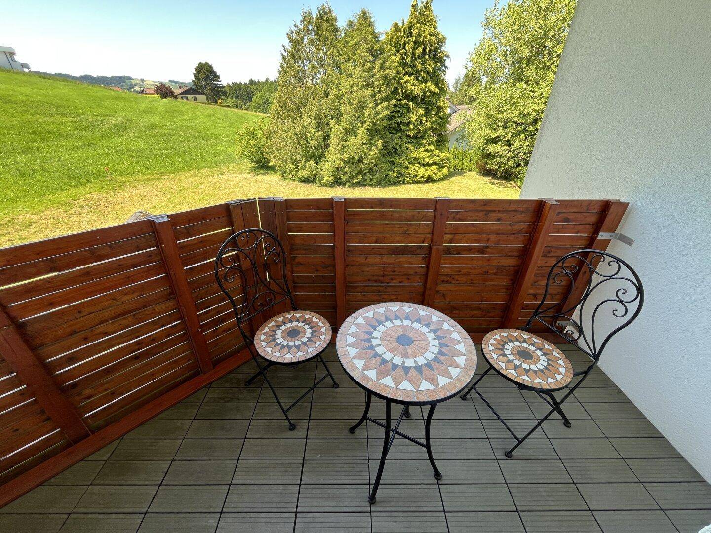 Kleiner Balkon mit Holzboden und Mosaiktisch, ideal für entspannte Stunden im Freien.