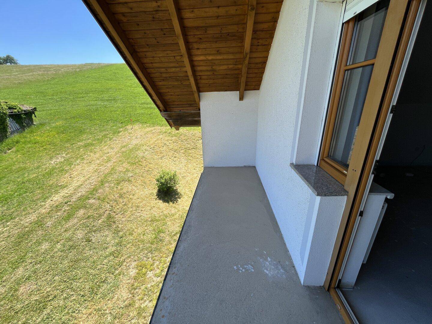 Überdachter Balkon mit Holzdach und weitem Blick auf die grüne Landschaft.