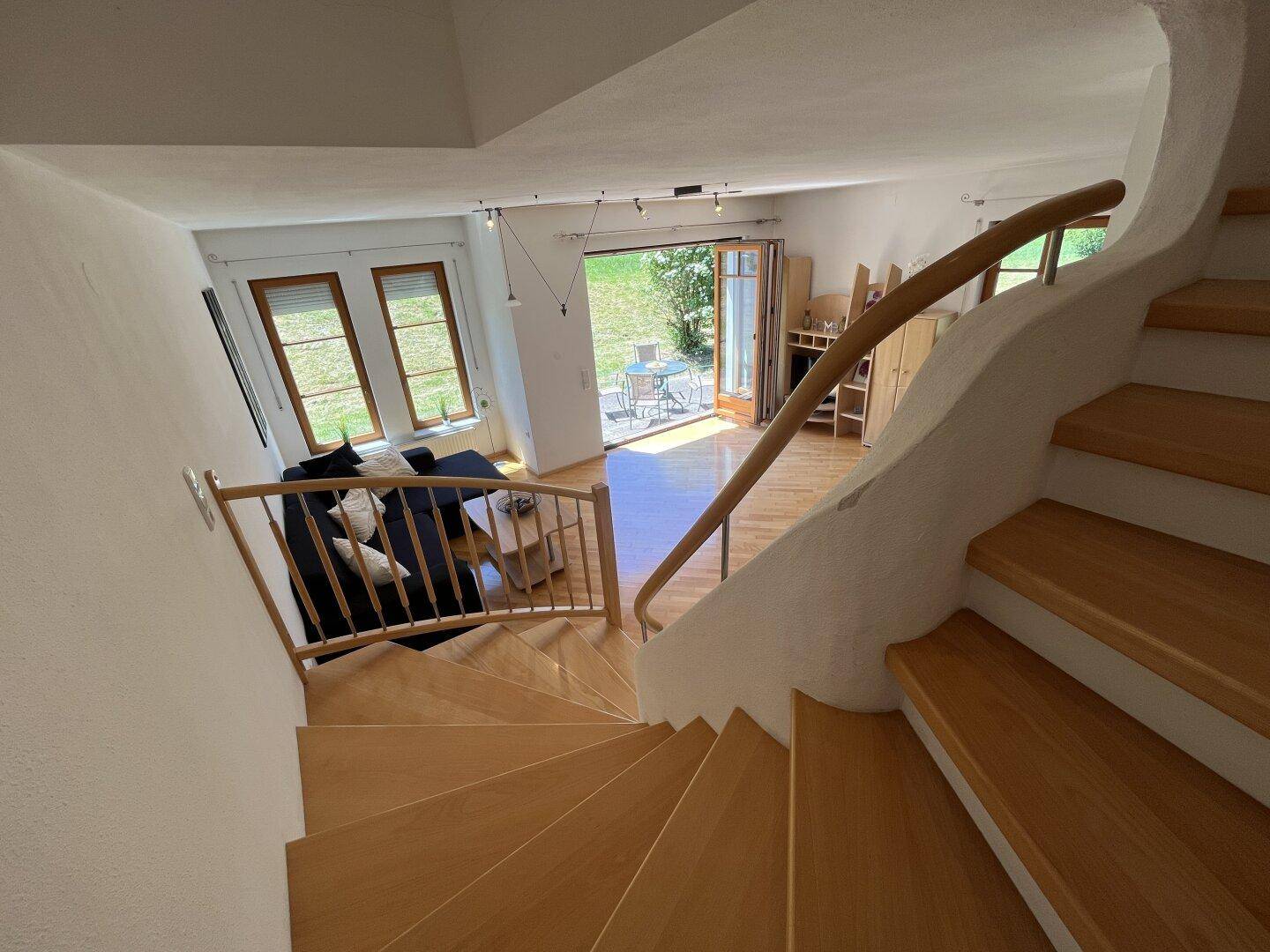 Blick vom Treppenaufgang in das helle Wohnzimmer mit Parkettboden und Terrassenzugang.