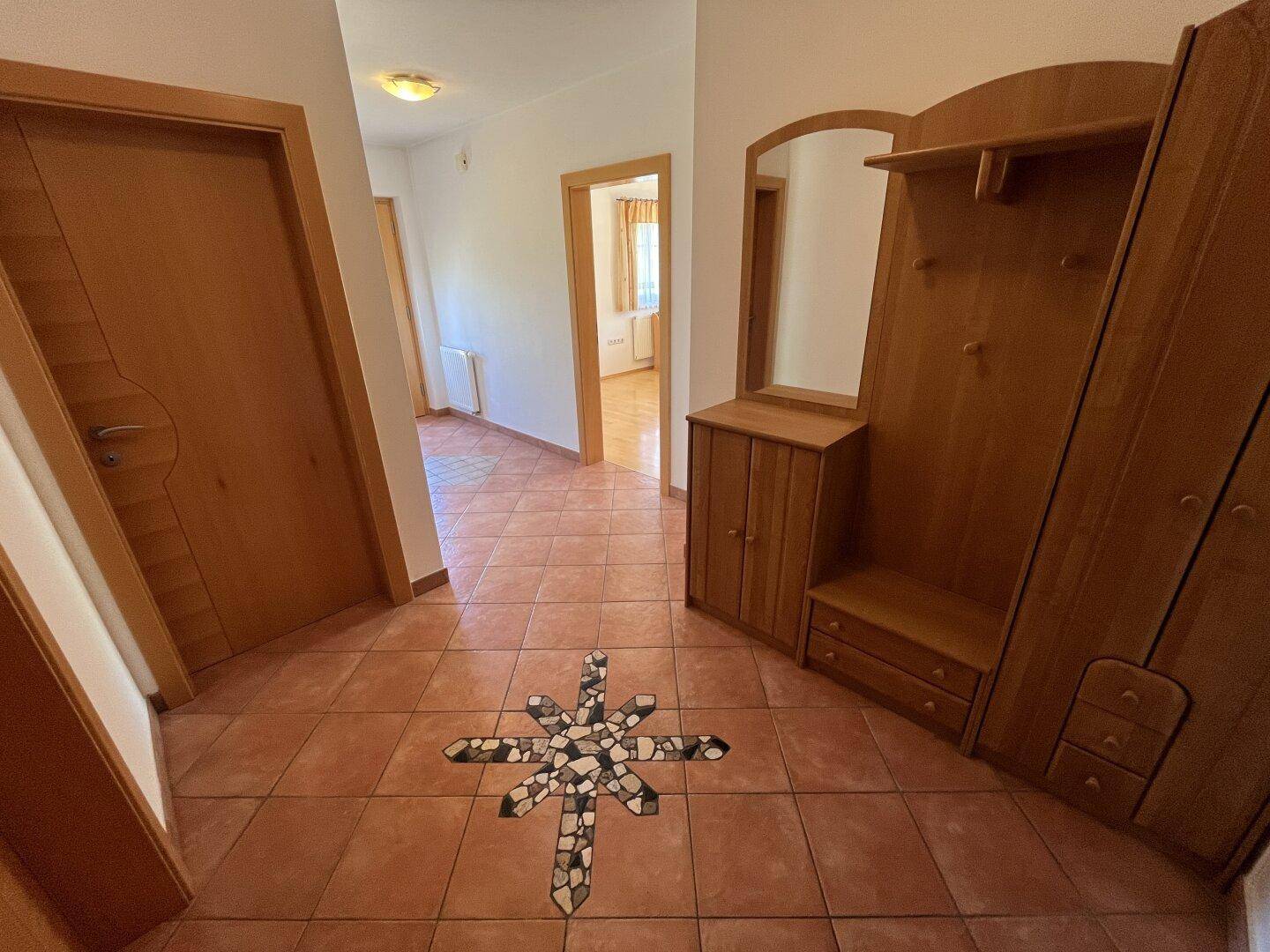 Heller Flur mit Terrakotta-Fliesen, Holztüren und einer Garderobe mit Spiegel.