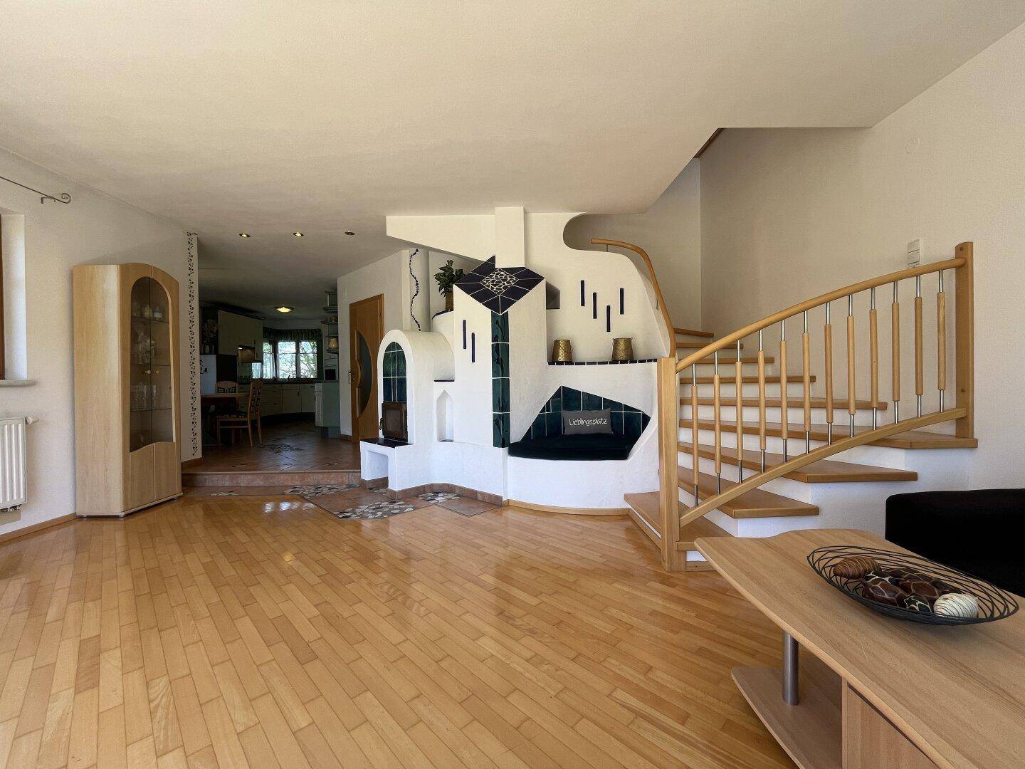 Helles Wohnzimmer mit Parkettboden, Kachelofen und offener Treppe zum Obergeschoss.