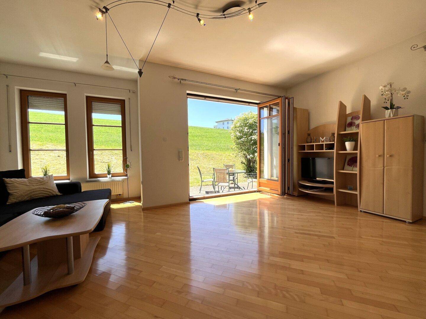 Lichtdurchflutetes Wohnzimmer mit Zugang zur Terrasse und Blick auf die grüne Landschaft.