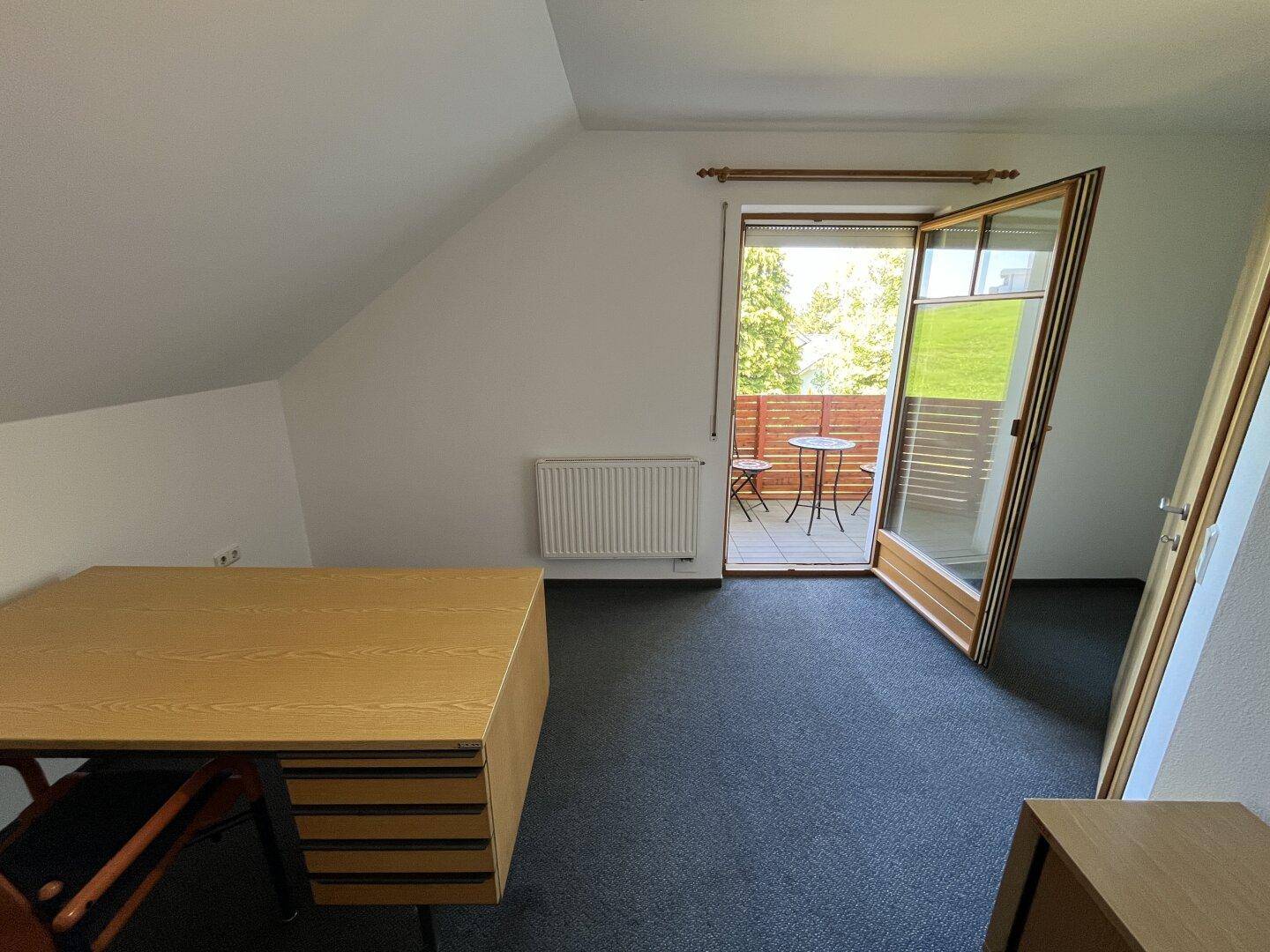 Arbeitszimmer mit Teppichboden, Schreibtisch und Zugang zu einem kleinen Balkon.