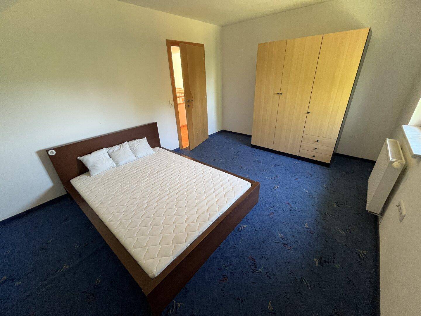 Schlafzimmer mit blauem Teppichboden, Doppelbett und großem Kleiderschrank.