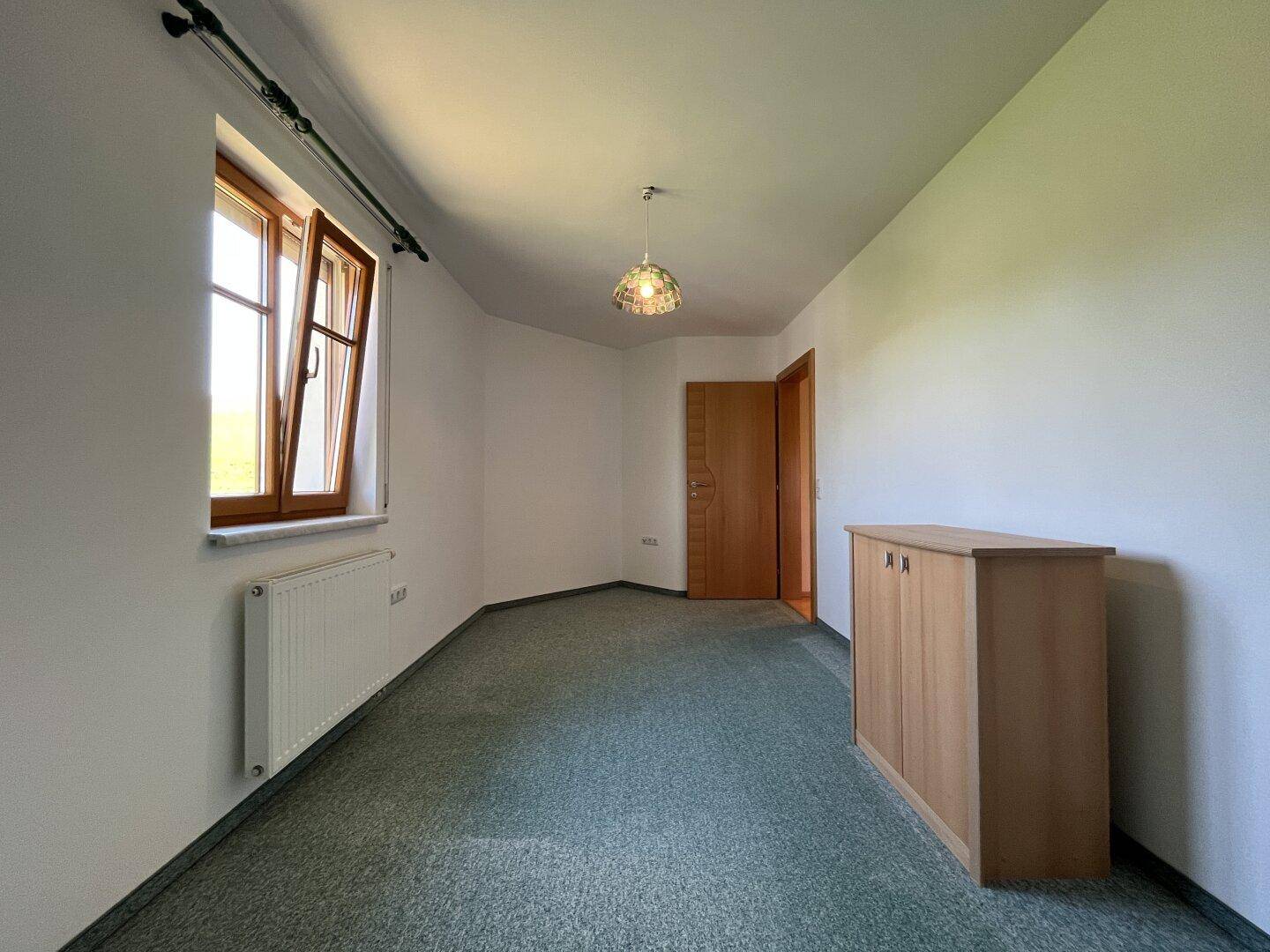 Helles Schlafzimmer mit grünem Teppichboden und Fenster mit Blick ins Grüne.