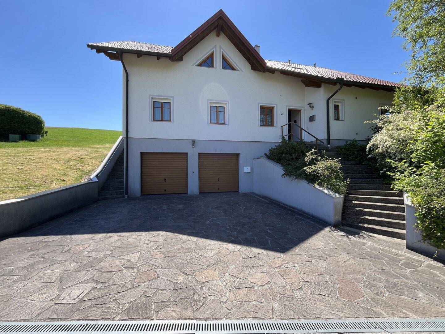 Vorderansicht des Hauses mit zwei Garagentoren und einer gepflasterten Zufahrt.