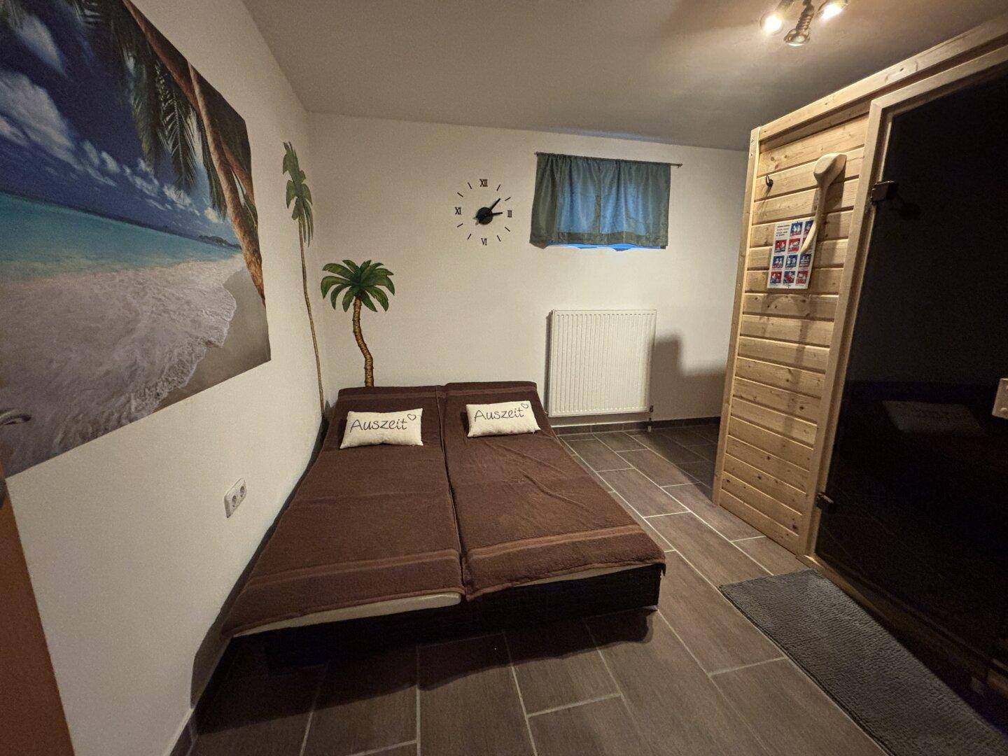 Raum mit zwei Liegen, einem Strandbild an der Wand und einer integrierten Sauna für Entspannung.