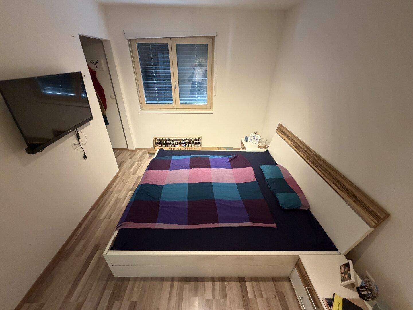 Schlafzimmer mit Laminatboden, Doppelbett und Wandfernseher, bietet direkten Zugang zu einem Ankleidebereich.