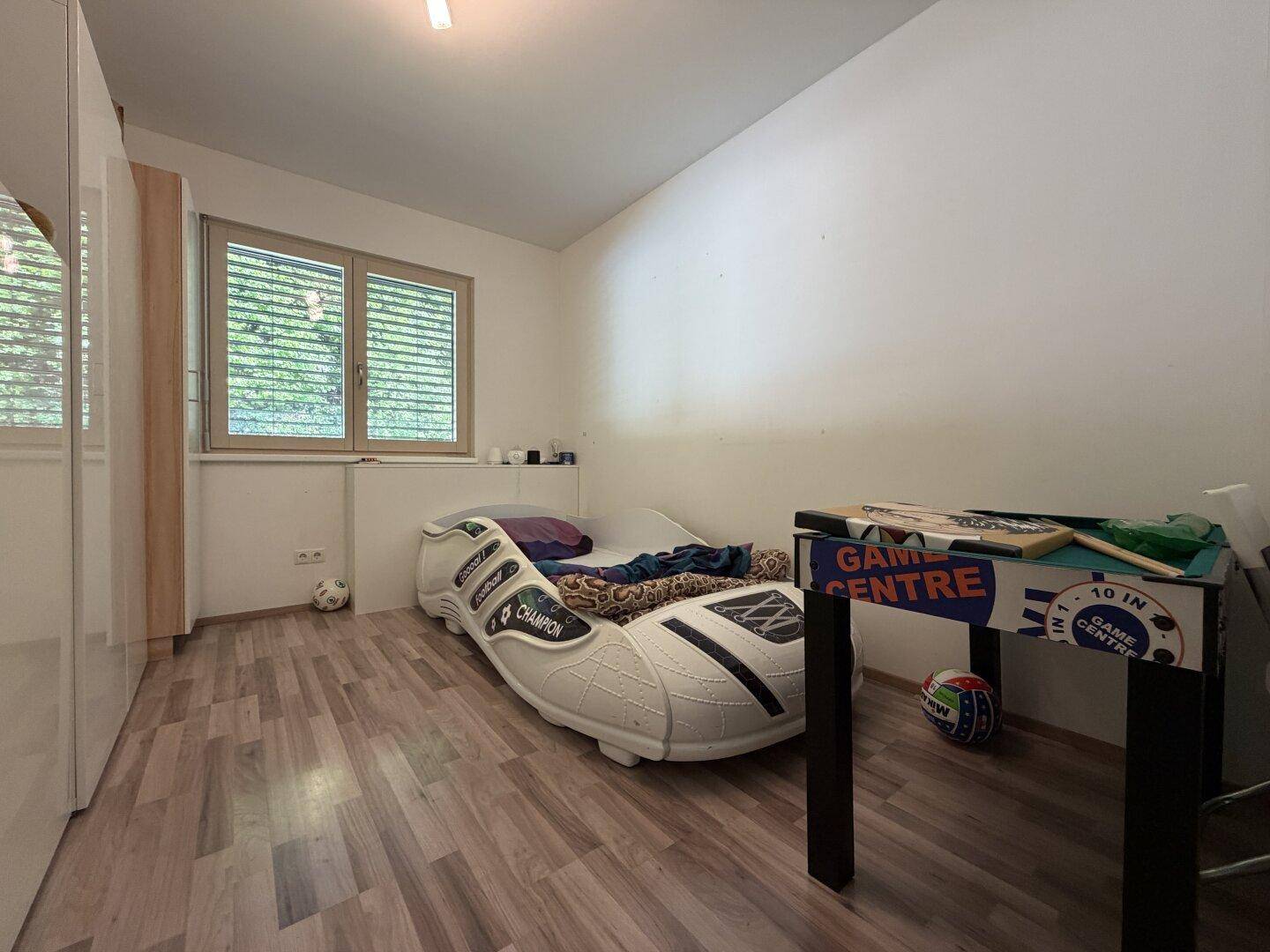 Kinderzimmer mit Laminatboden, Fenster und einem einzigartigen Bett in Form eines Sportschuhs.