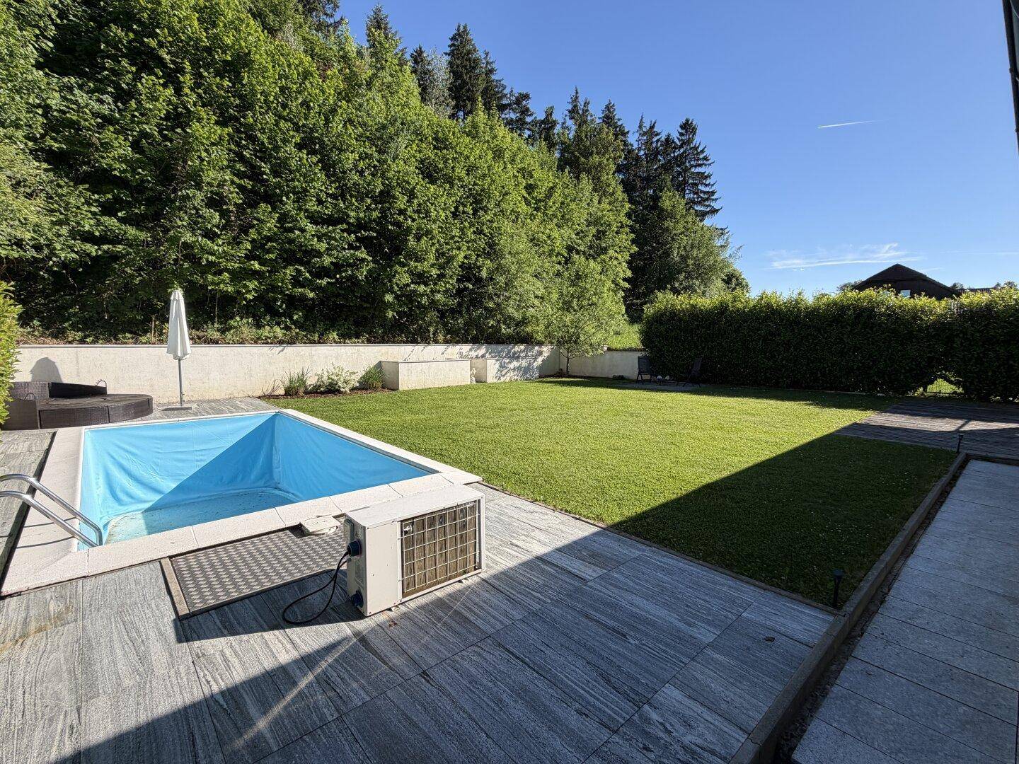 Entspannender Gartenbereich mit Swimmingpool, gefliester Terrasse und umgebender Hecke.