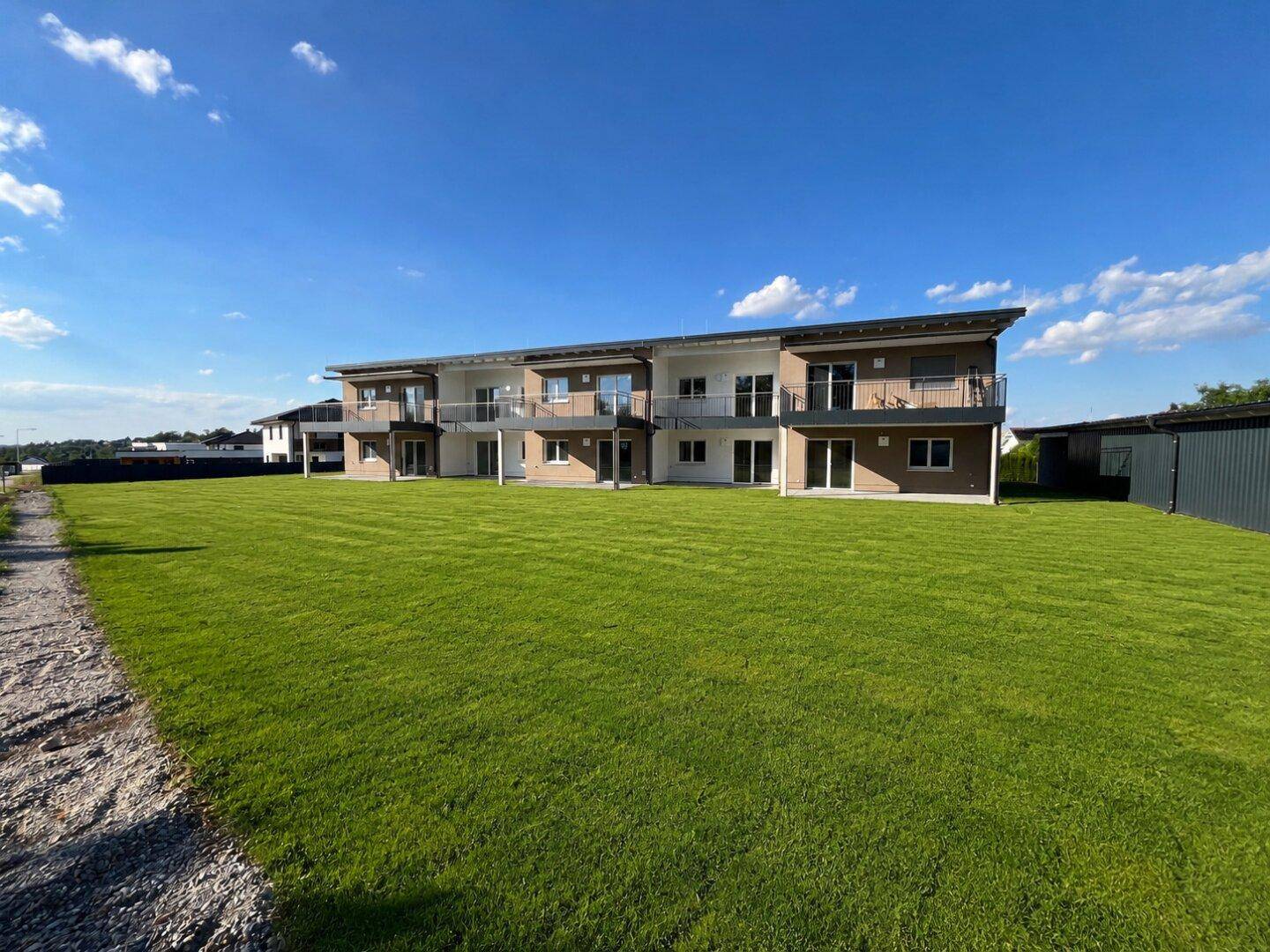 Modernes Mehrfamilienhaus mit Balkonen und großzügiger Rasenfläche unter blauem Himmel.