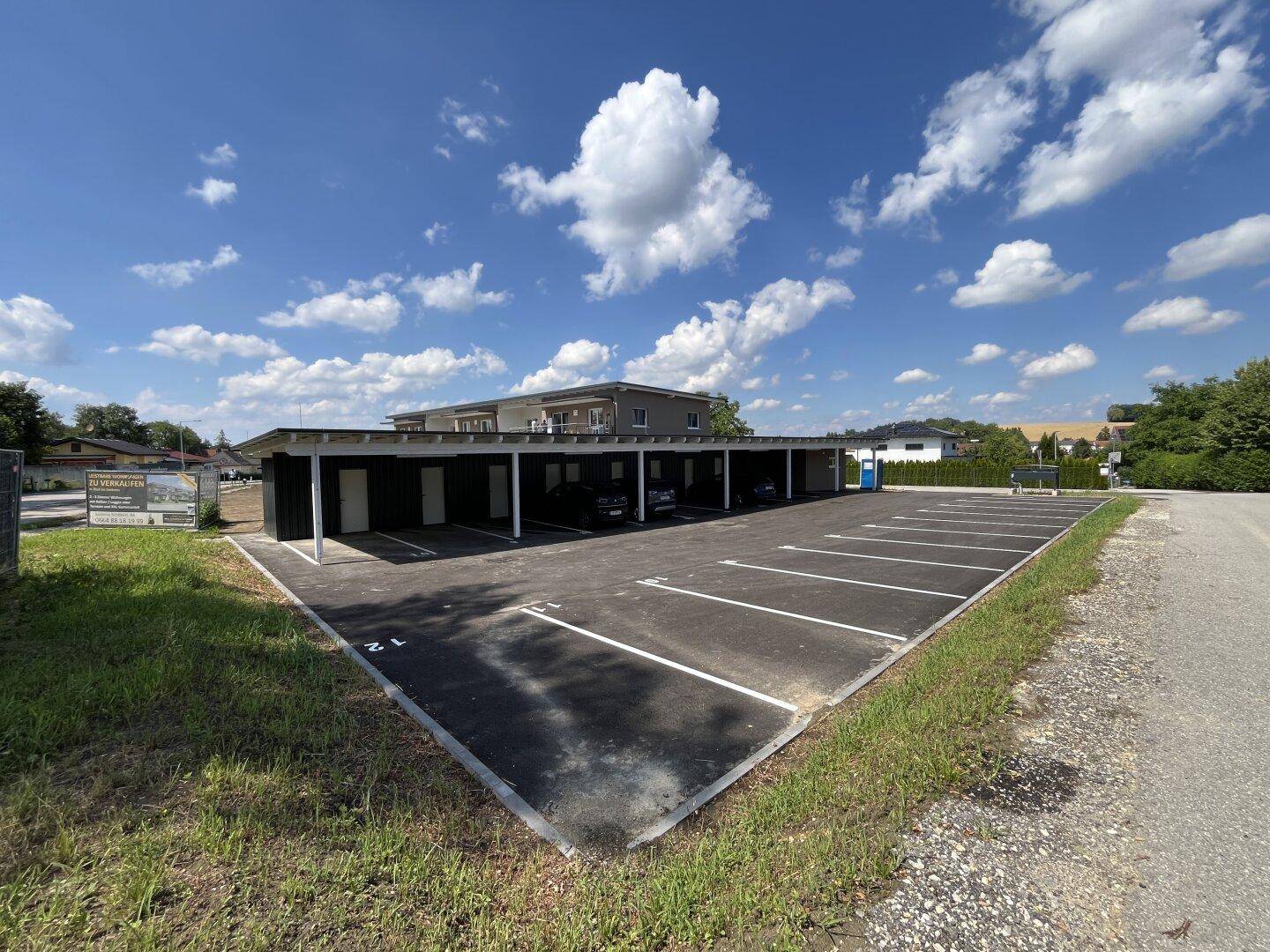 Großer Parkplatz mit Carport-Anlage neben dem modernen Wohngebäude.