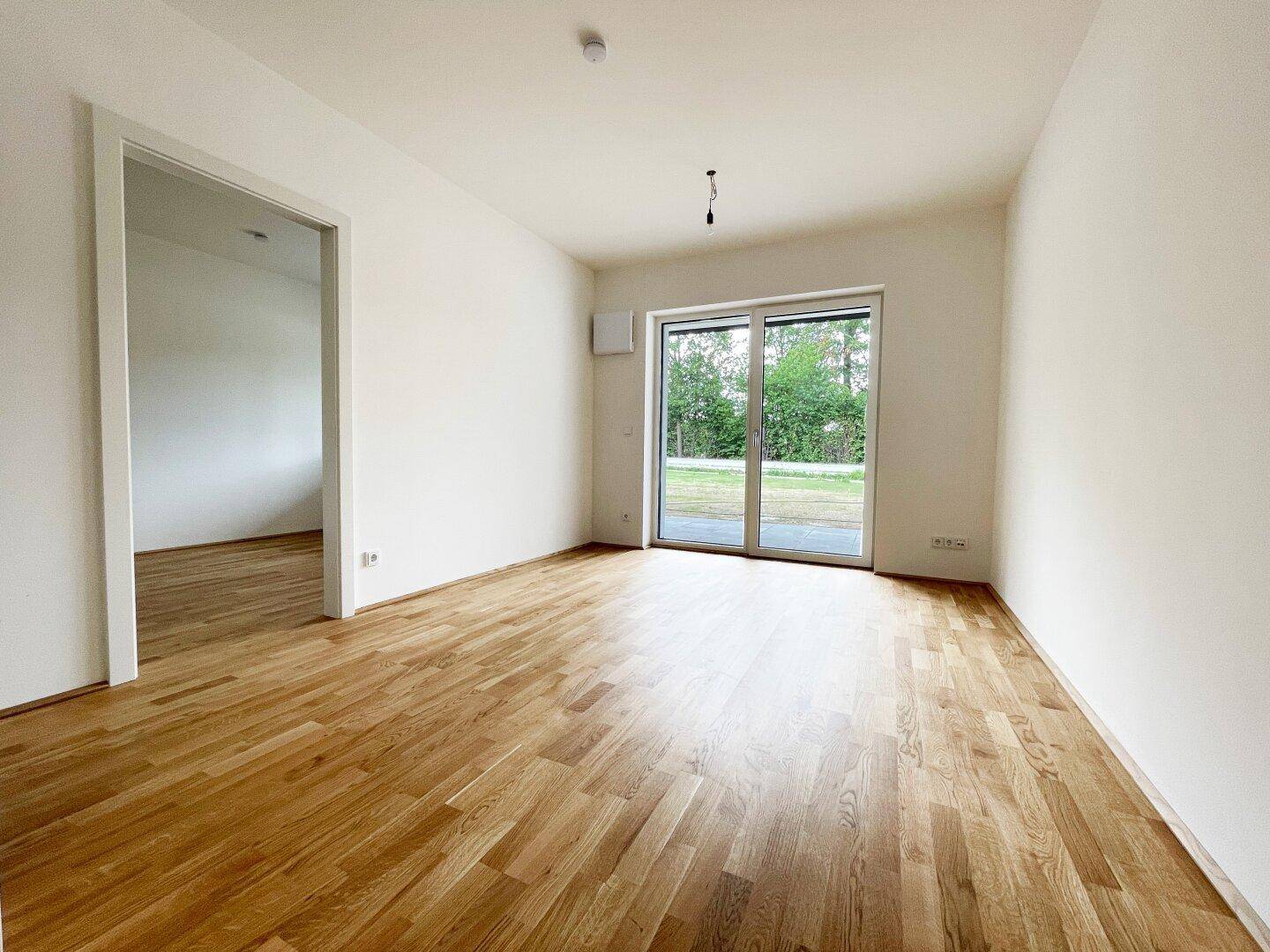 Helles, unmöbliertes Wohnzimmer mit Parkettboden und großzügigem Zugang zu einer Terrasse oder Garten.