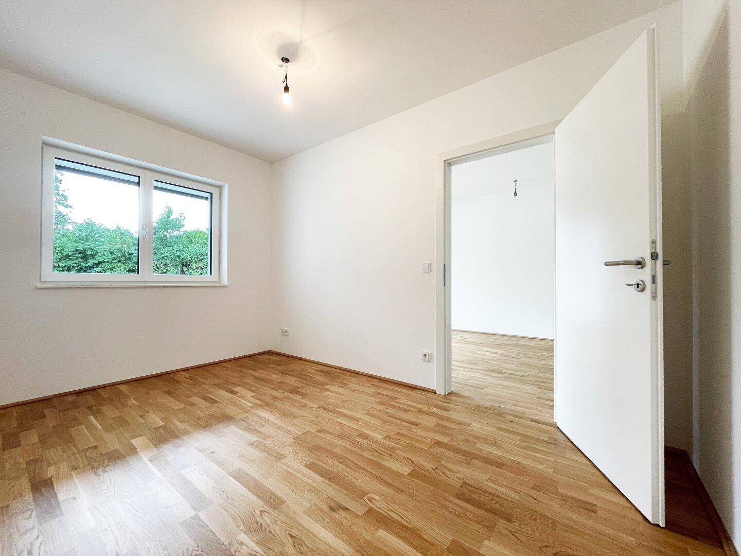 Helles Schlafzimmer mit Parkettboden und Fenster, das einen angenehmen Blick ins Grüne bietet.