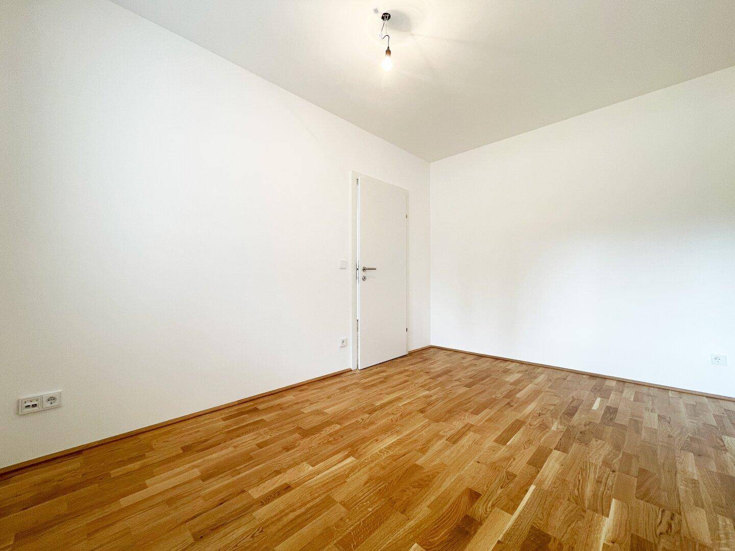 Leeres Schlafzimmer mit Holzboden und weißen Wänden, bereit für individuelle Gestaltung und Möbel.