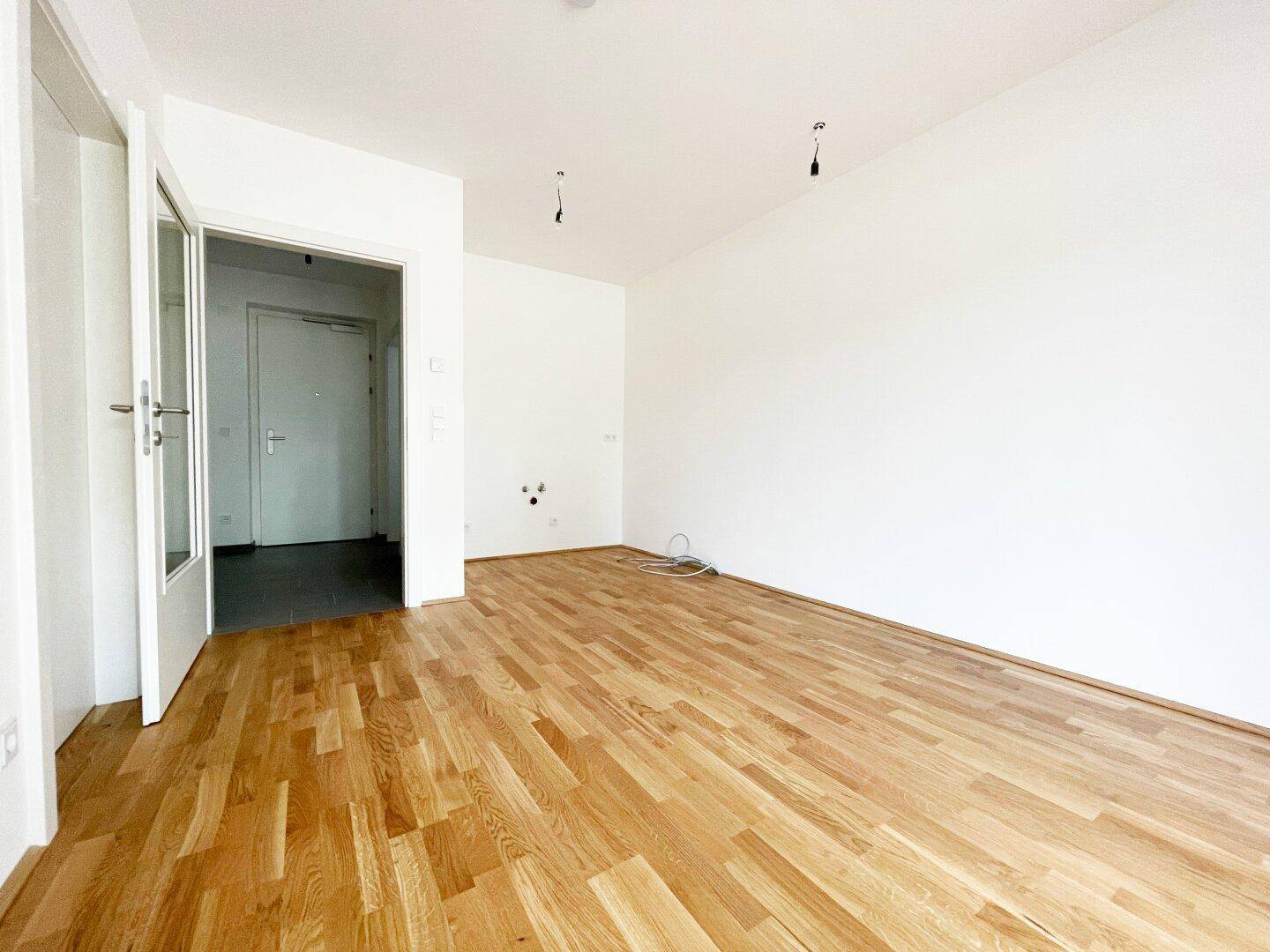 Geräumiges, leeres Zimmer mit Holzboden und weiß gestrichenen Wänden, bereit zur Einrichtung.