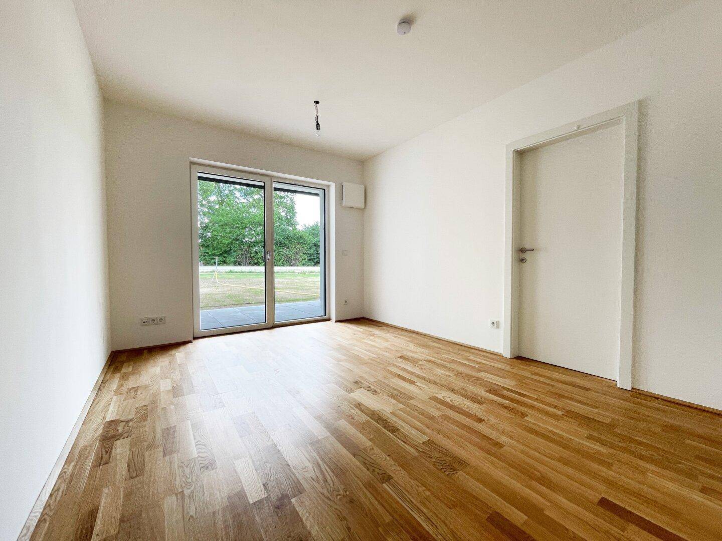 Helles Zimmer mit Holzboden und großen Schiebetüren, die Zugang zum Garten bieten.