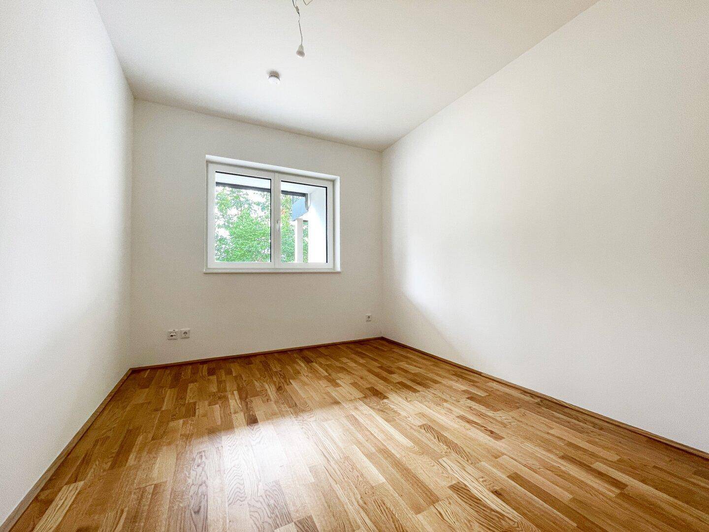 Ruhiges Zimmer mit Holzboden und einem Fenster, das viel Tageslicht hereinlässt.