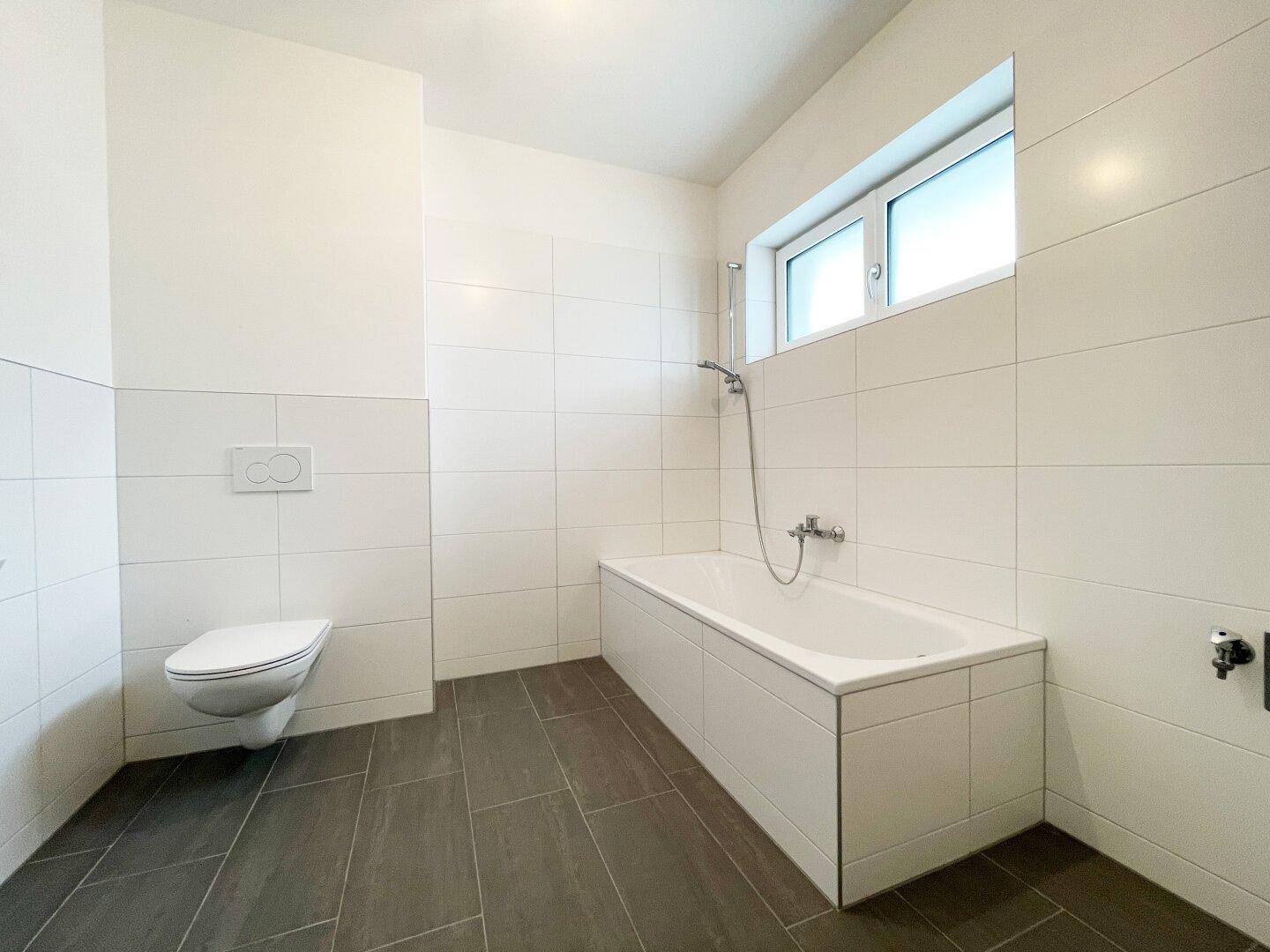 Modernes Badezimmer mit Badewanne, wandhängendem WC und großformatigen Fliesen.