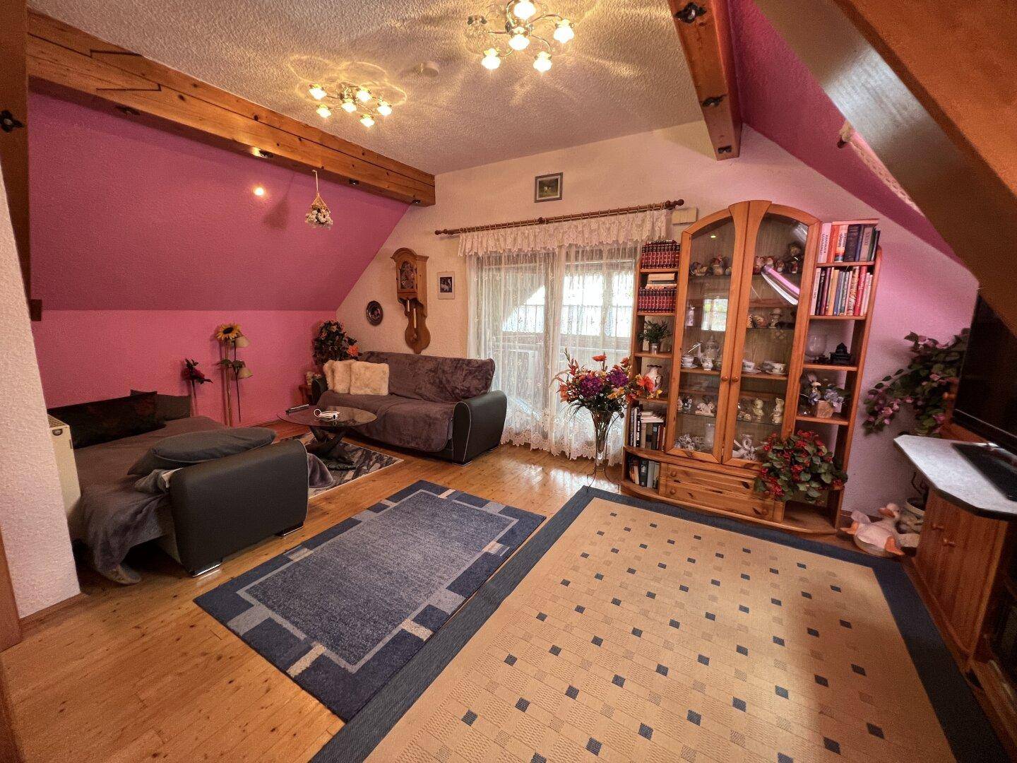 Geräumiges Wohnzimmer im Dachgeschoss mit Holzbalken und pinkfarbenen Wänden.