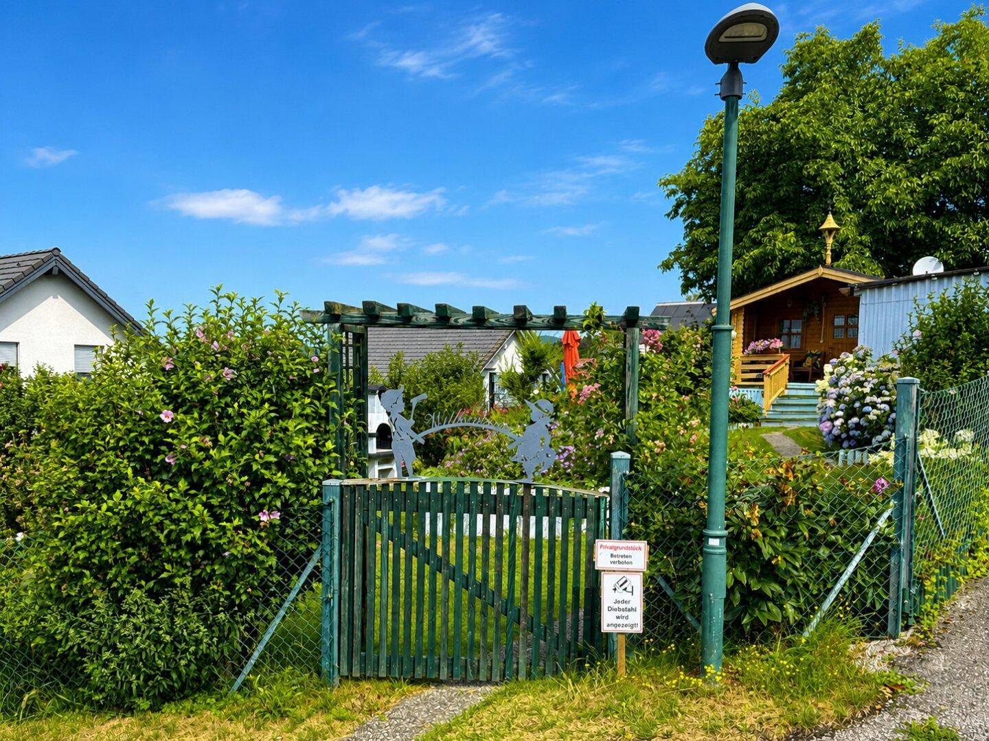 Grüner Gartenzaun mit dekorativen Figuren und üppiger Bepflanzung im Vordergrund.